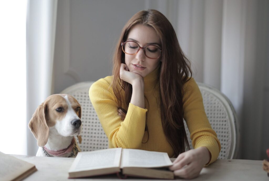 Young woman reading a book with her dog beside her indoors.